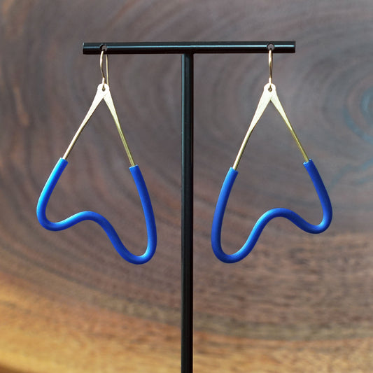 A pair of blue MCM style earrings with brass wire and gold-filled hooks, displayed on a black T-stand against a dark wood background by artist Jacki Geary with JAX Atelier.