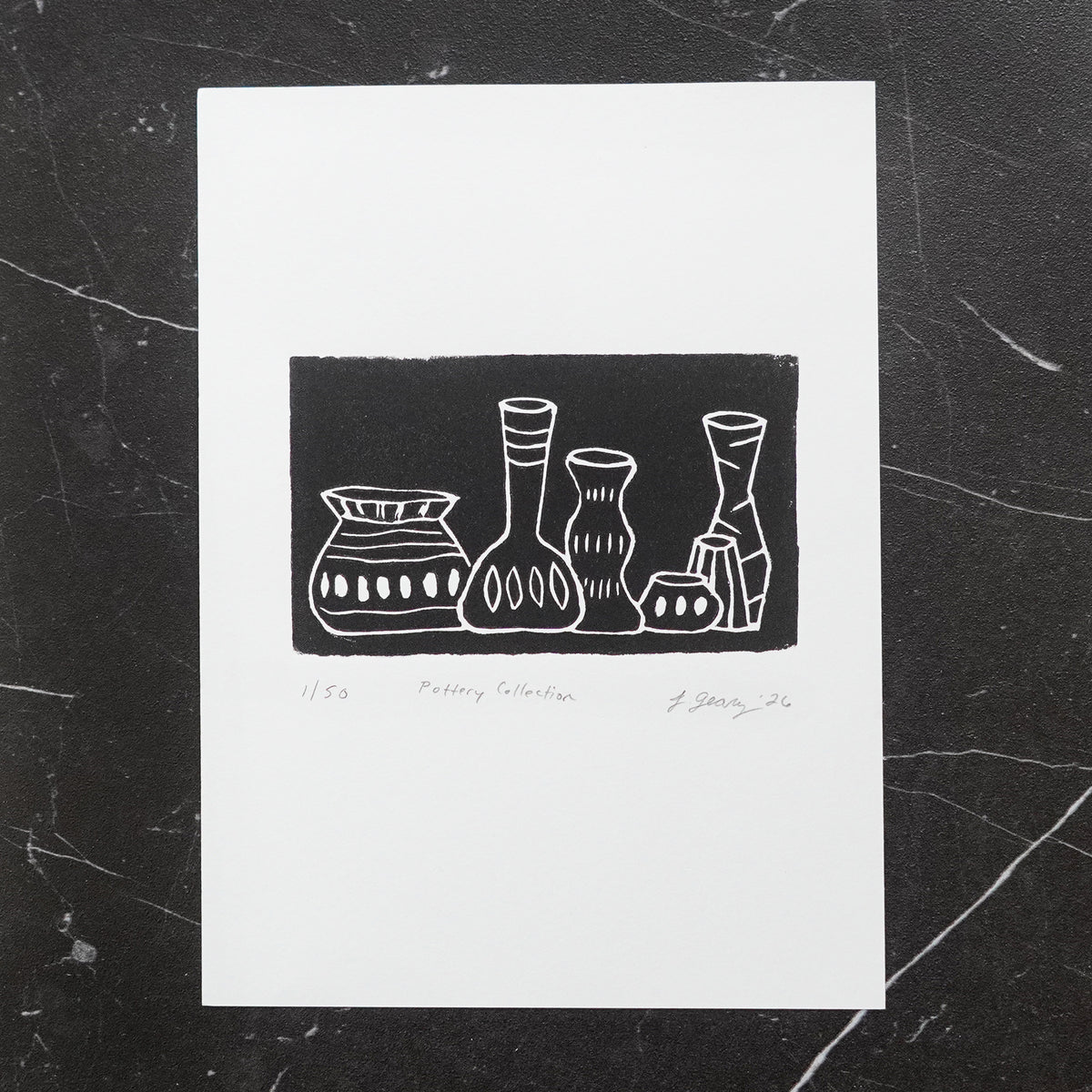A black and white linocut limited edition print titled 'Pottery Collection' featuring a minimalist illustration of five vases, displayed on a dark marble surface. By Jax Atelier in San Diego.