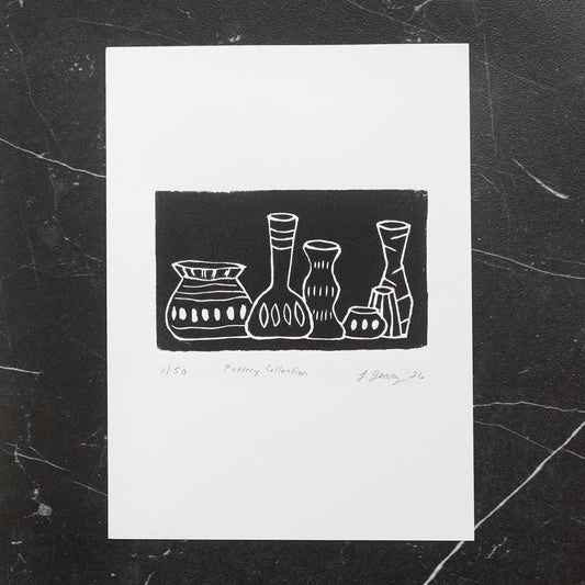 A black and white linocut limited edition print titled 'Pottery Collection' featuring a minimalist illustration of five vases, displayed on a dark marble surface. By Jax Atelier in San Diego.