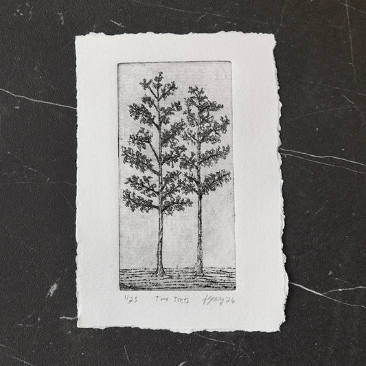 A black and white drypoint etching of two trees on deckled edge white watercolor paper, displayed on a dark marbled tile surface. By Jax Atelier in San DIego.